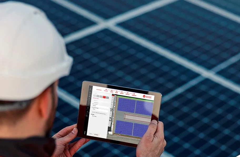 Monteur mit Helm prüft die Dachplanung auf dem Tablet, im Hintergrund Solarmodule