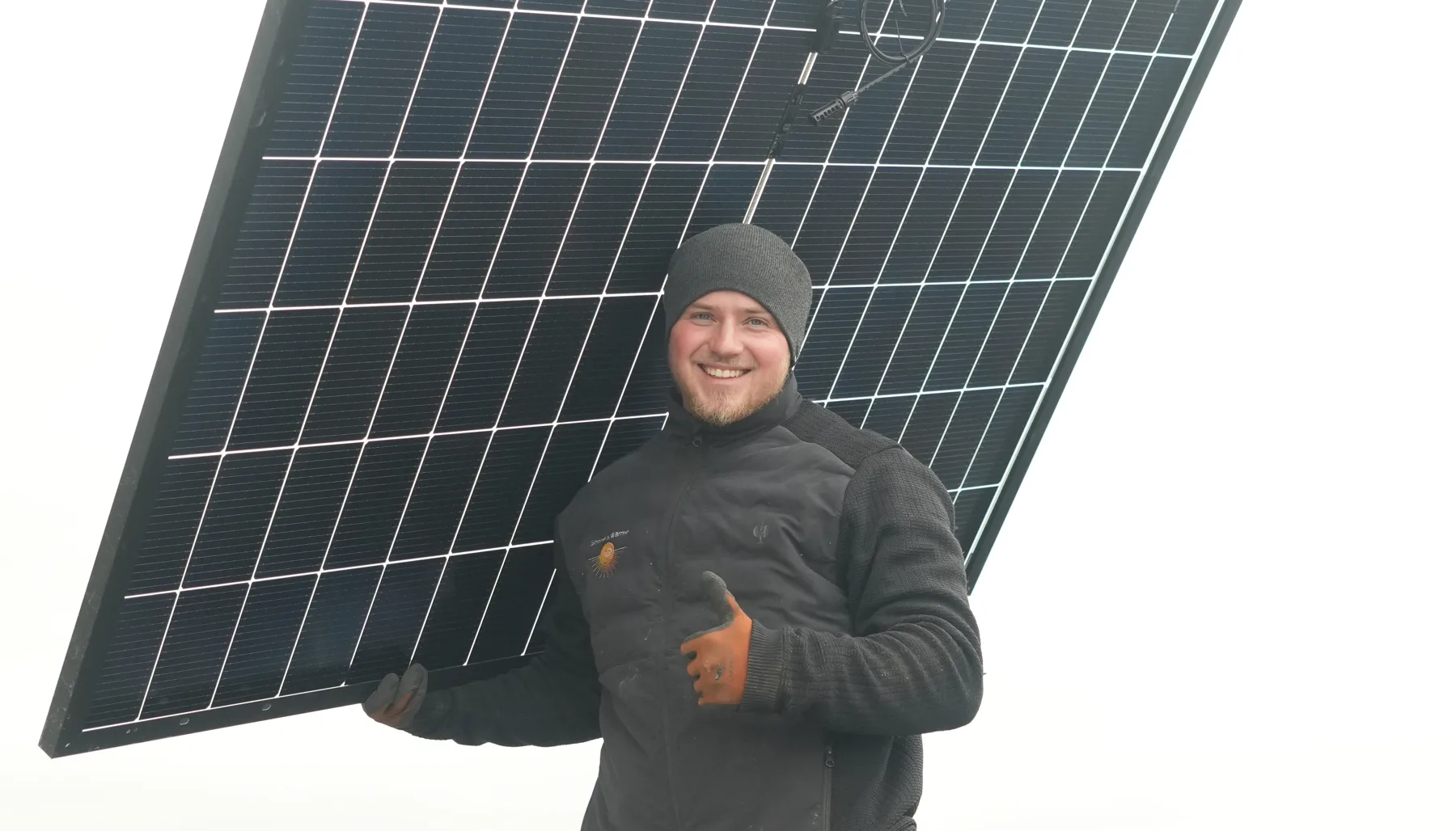 Monteur von Sonne & Wärme trägt ein Solarmodul über das Dach